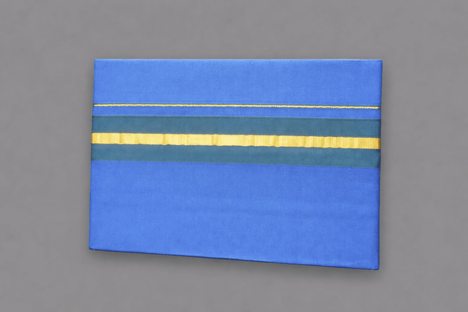 Dark Blue Pure Cotton Dhoti with Green & Gold Stripe | Traditional South Indian Pancha Dark blue pure cotton dhoti with horizontal green and gold stripe, neatly folded South Indian traditional pancha on a grey background